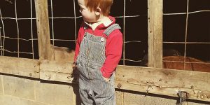 Rye Withington wearing a red shirt and shoes with blue bibbed overalls