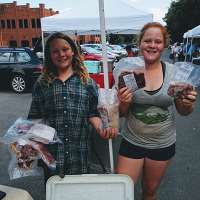 Dennet and Lilly holding up meats products for sale at the market