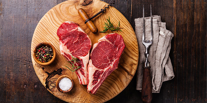 Raw Steaks On A Cutting Board With Salt And Pepper And A Cork Screw